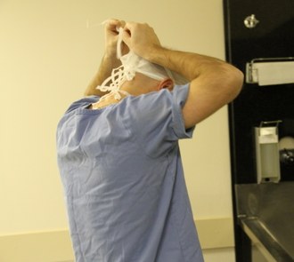 Homem, de costas, amarra a máscara cirúrgica