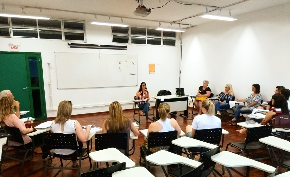 Foto com grupo de professores sentados em círculo, com uma professora falando para a equipe