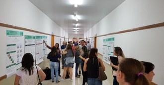 Na imagem um corredor onde vários trabalhos estão posicionados nas paredes e estudantes realizam apresentações de banners simultaneamente.