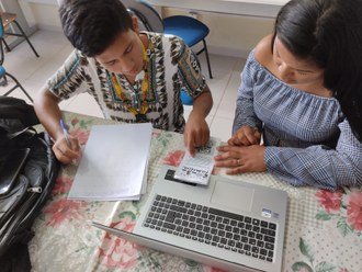 Foto registra dois estudantes indígenas revisando o conteúdo do folder.
