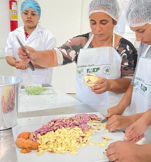 Foto mostra três mulheres descascando e cortando batata doce para a preparação dos alimentos.