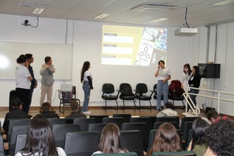 Na foto um grupo de estudantes realiza uma apresentação para a plateia no auditório.