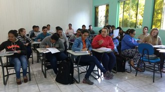 Pessoas sentadas em suas carteiras, em uma sala, durante aula.