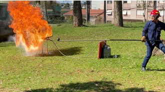 foto de uma pessoa lidando com um equipamento contra incêndio e do lado dela uma chama de fogo