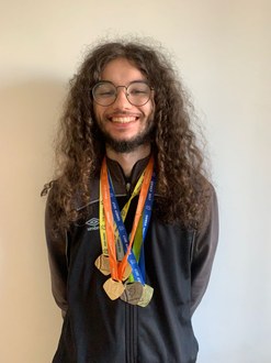 foto de um estudante sorrindo com várias medalhas no pescoço