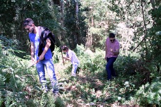 Em meio à mata, Natan está à esquerda, Diluan mais atrás, no meio, e Marcelo à direita, com ferramentas nas mãos, cortando alguns galhos e tirando algumas vegetações rasteiras para o espaço da trilha
