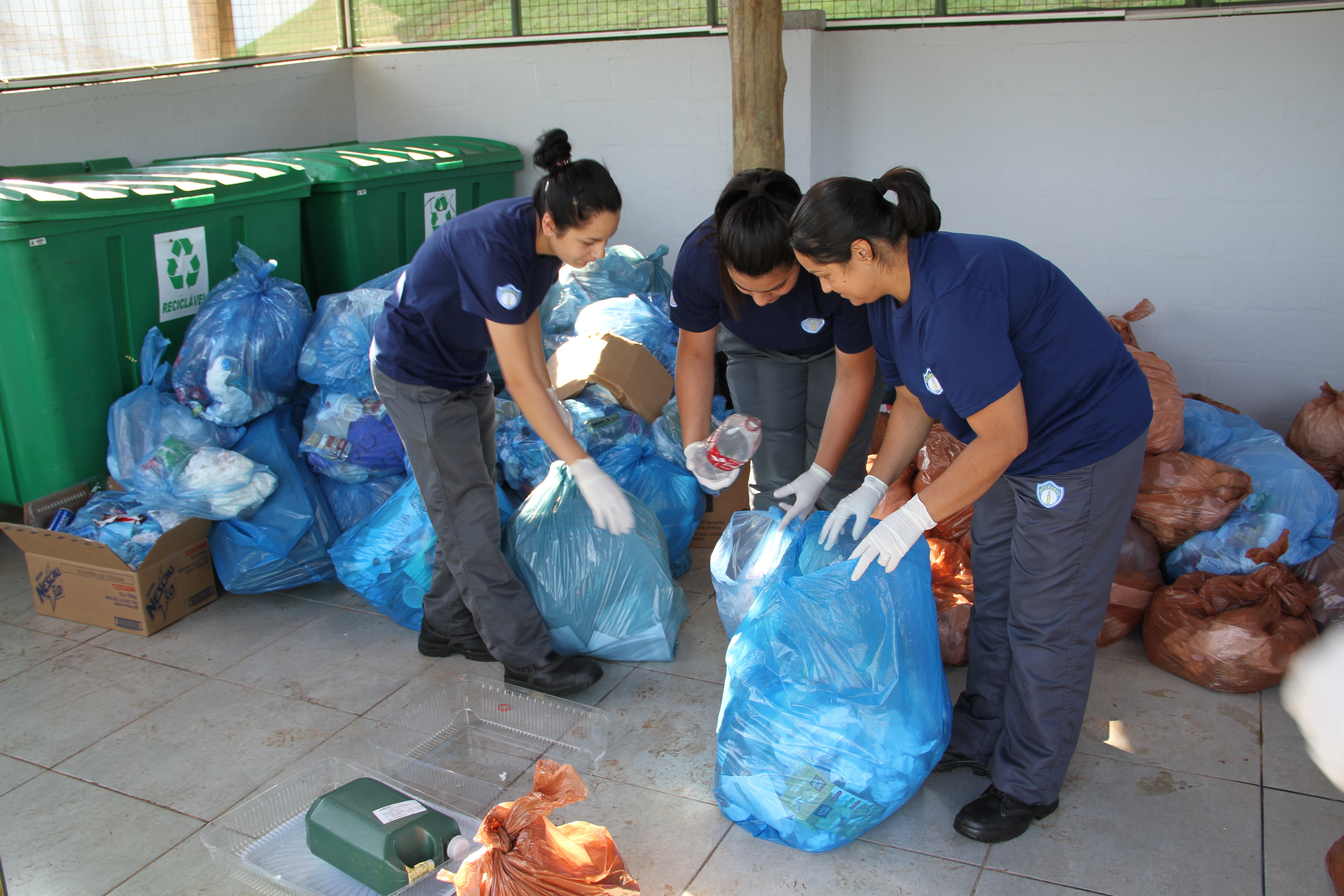 Na frente de muitos sacos de lixo cheios, três mulheres fazem a separação do lixo de um dos sacos