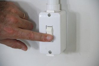 Em plano fechado, interruptor é tocado por mão, apagando as luzes