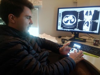 Venson está em frente a um computador, segurando um smartphone com imagens de exames