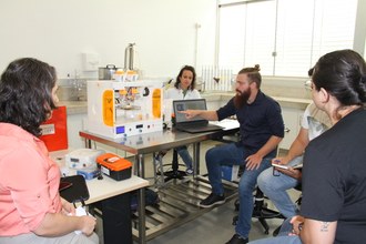 Na foto várias pessoas acompanham a explicação sobre o uso da bioimpressora 3D.