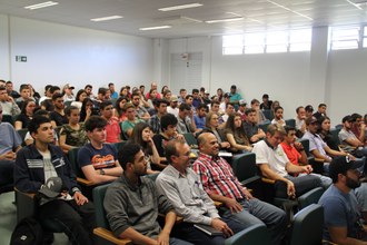 Na imagem os participantes sentados no auditório assistem a apresentação do palestrante.