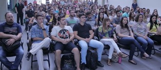 Foto em plano aberto mostrando os alunos sentados em cadeiras em fila de frente para a câmera