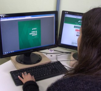 Uma pessoa, fotografada de costas, olha para o arquivo da carta de serviços ao usuário em seu computador