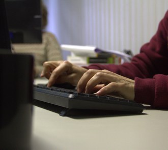 Foto, em ângulo fechado, de duas mãos sobre um teclado de computador